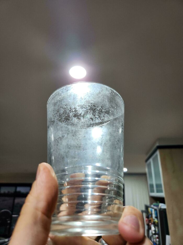 A hand holding a cloudy glass, likely with hard water stains, seeking help fixing things and finding answers to problems.