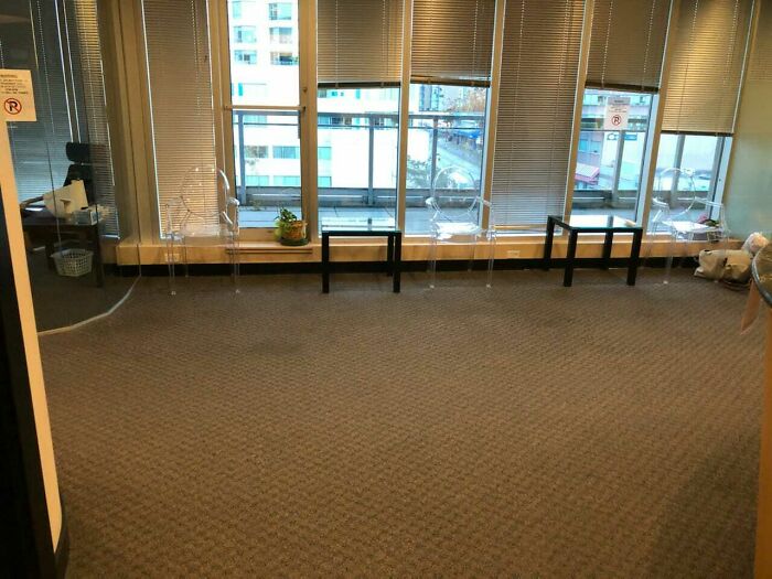A poorly designed office space with construction fails, featuring misaligned chairs and tables next to large windows.