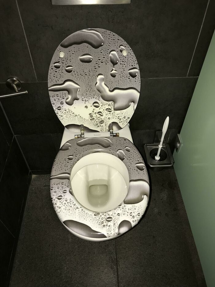 A construction fail: a toilet seat with a misleading water drop design, appearing wet, in a modern bathroom.