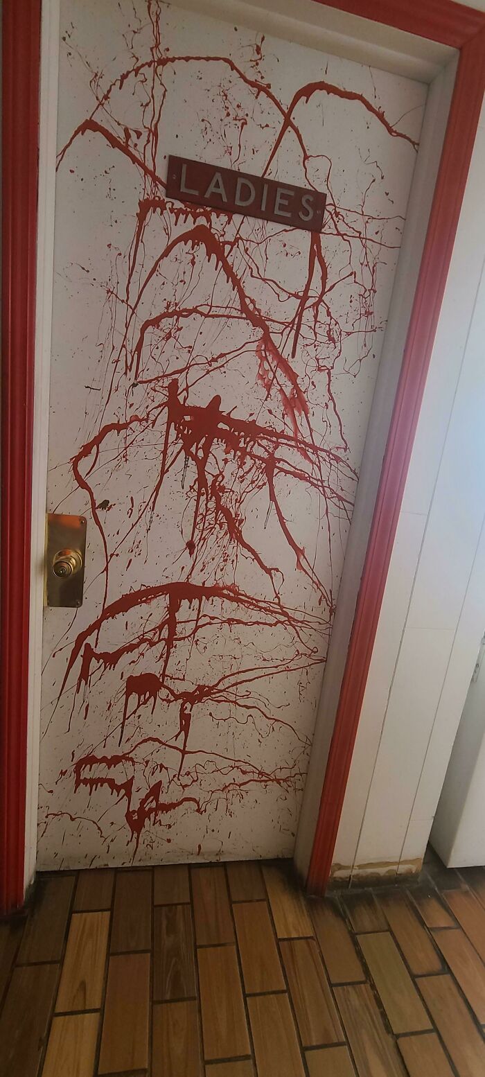 A white ladies room door splattered with red paint resembling blood, a peculiar construction fail.