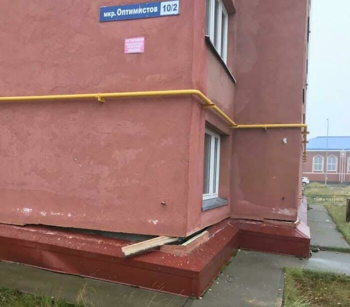 The base of a reddish building showing a clear gap and exposed wood, an example of construction fails.
