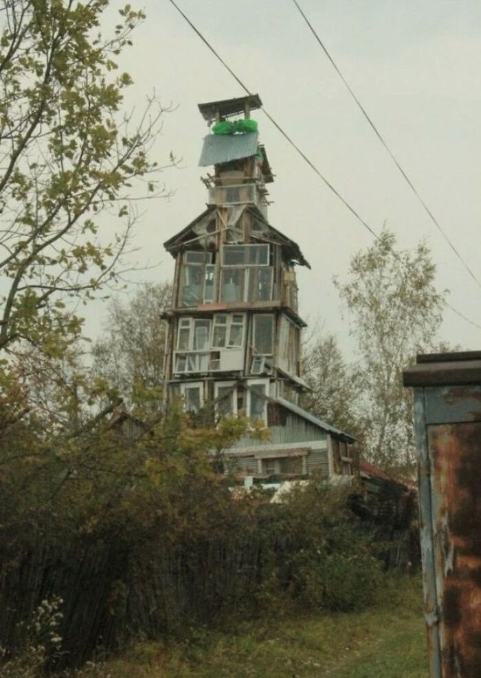 A hilariously tall, rickety house made of mismatched windows, a true construction fail in the forest.