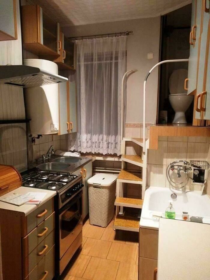 A toilet installed high above a kitchen area, accessed by stairs, a bizarre construction fail.