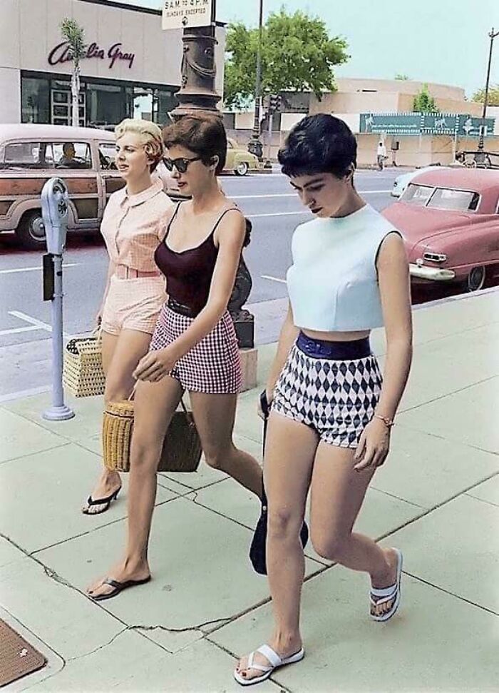 Historical photo of three women in shorts walking down a street, reflecting fashion and life from a past era.
