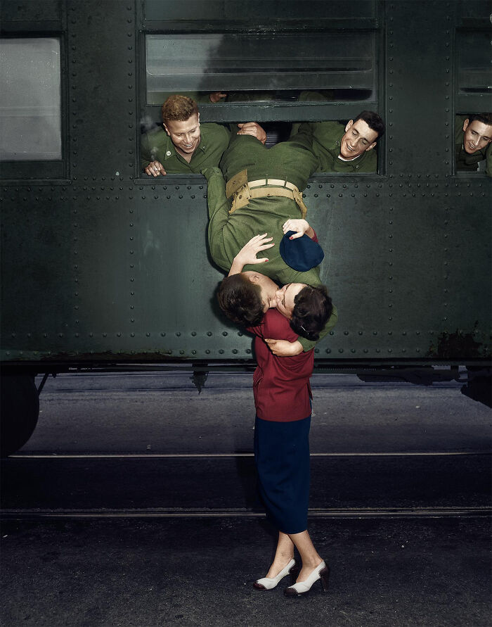 Historical photo of a soldier hanging upside down from a train window to kiss a woman goodbye, capturing a poignant past moment.