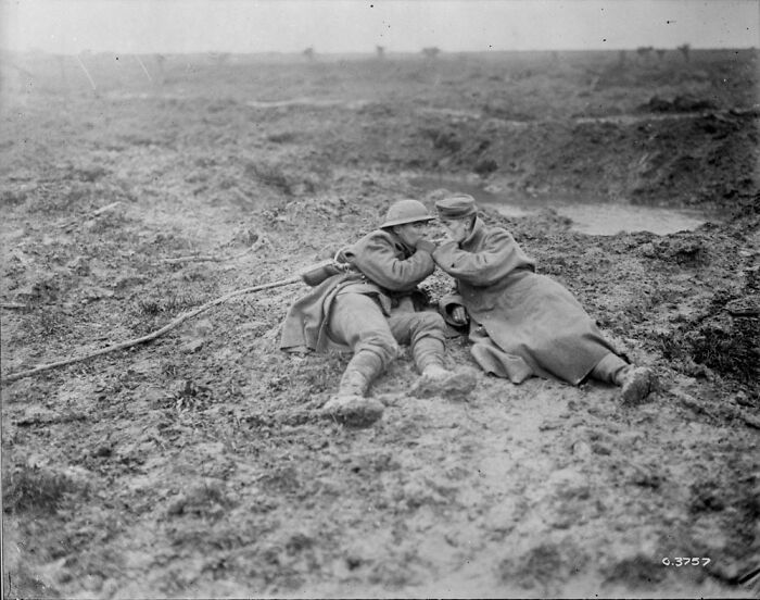 Historical photo of two soldiers communicating in a muddy trench, showing the harsh realities of past warfare.