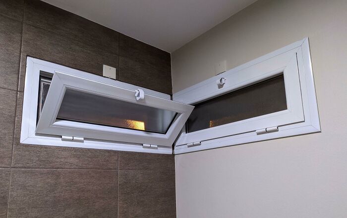 Two small, high windows in a corner, with one poorly installed and unable to close properly, a construction fail.