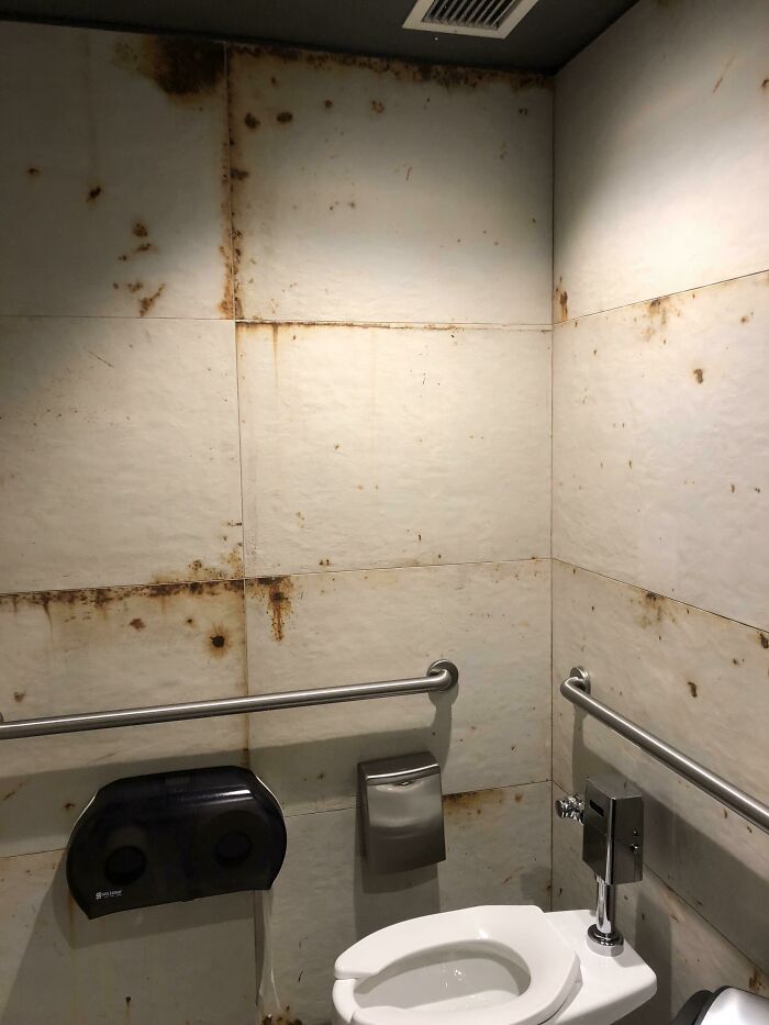 A bathroom with construction fails: rust-colored stains on the white tiled walls.