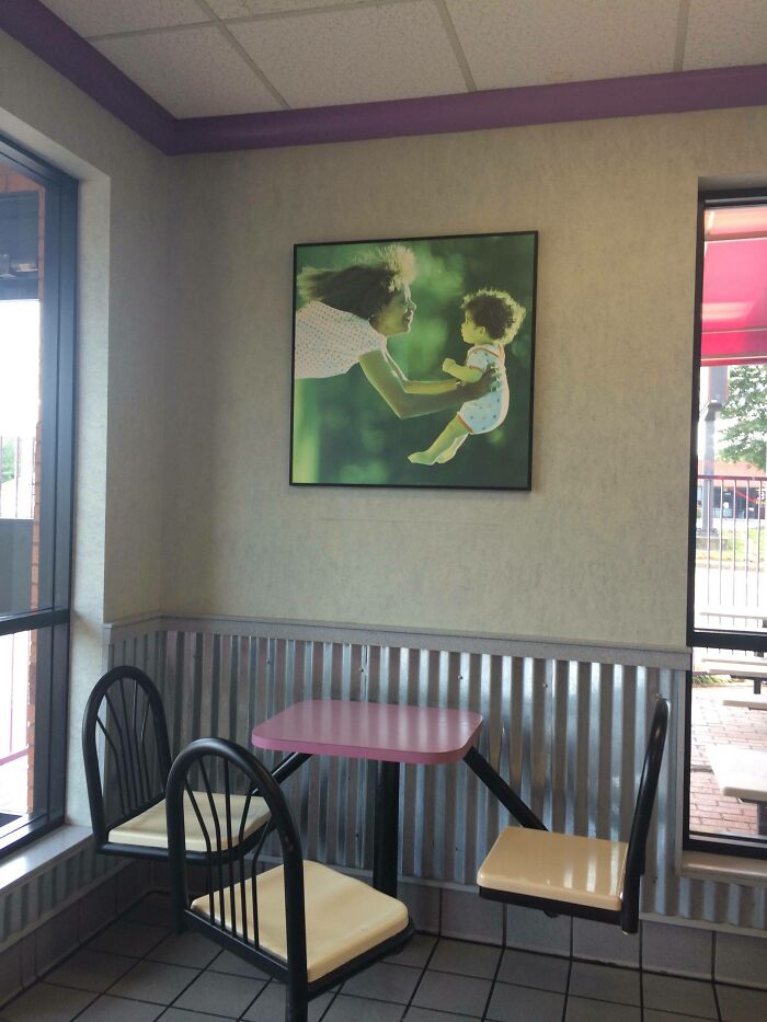 A small dining area with a pink table and two chairs, featuring a framed image on the wall, hinting at a construction fail in decor.