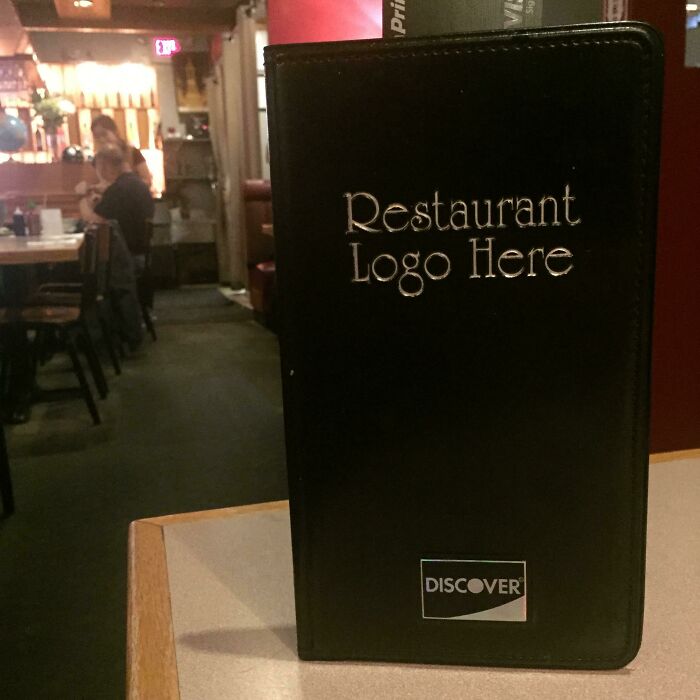 A black payment folder on a table with the text 'Restaurant Logo Here' and 'DISCOVER', an example of a branding construction fail.