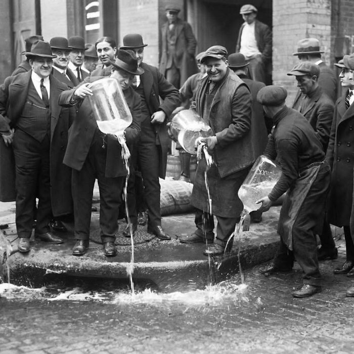 Historical photos: Men pouring liquid from large jugs onto a street, showcasing a moment from the past.