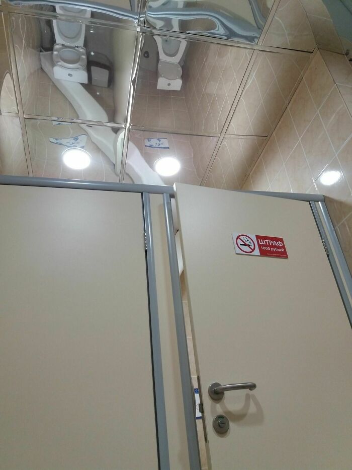 A public restroom with mirrored ceiling tiles reflecting toilets, a peculiar construction fail.