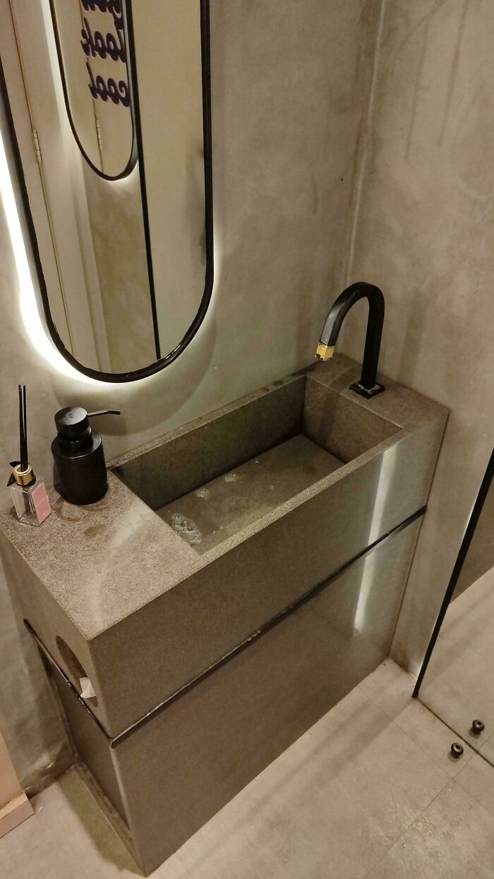 A bathroom sink with a unique design, featuring a black faucet, demonstrating a possible construction fail in functionality.
