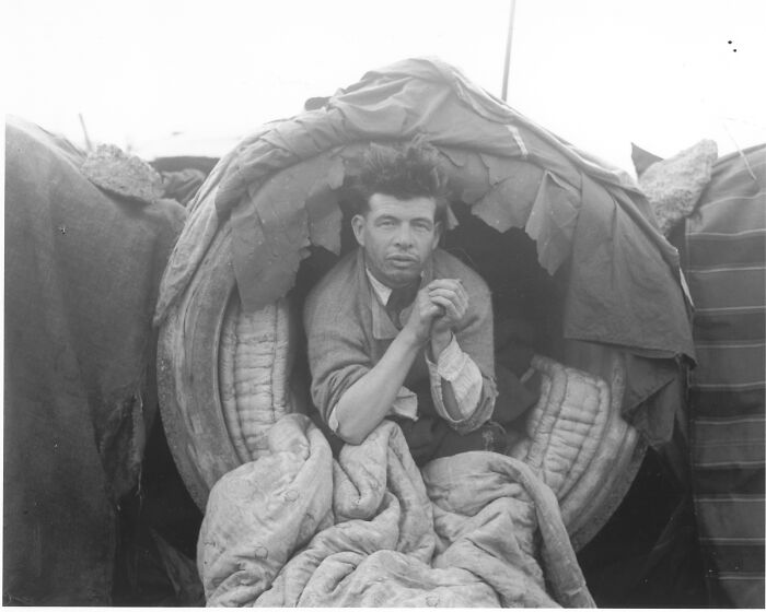 Historical photos: A man sits inside a makeshift shelter, his hands clasped, showing a past struggle.