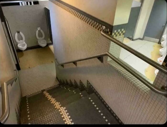 A staircase leading down to two exposed toilets without stalls, a prime example of construction fails in public restrooms.