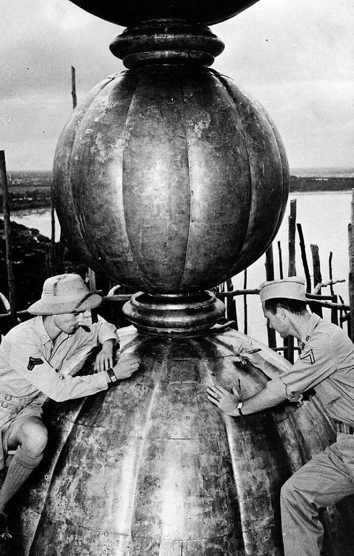 A historical photo of two men in military uniforms inspecting a large, ornate metal sphere outdoors.
