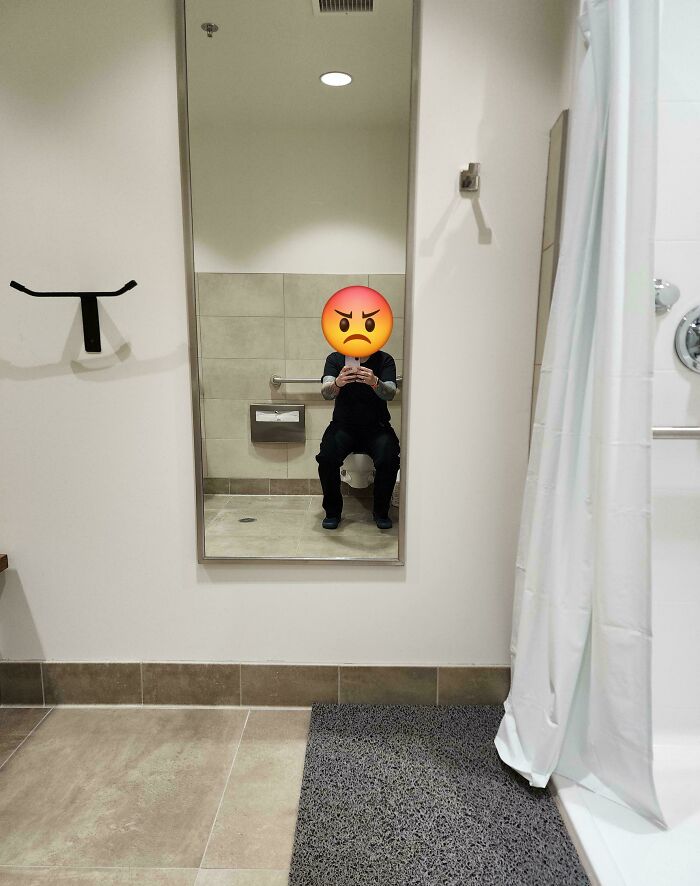A man reflecting an angry emoji in a mirror above an inconveniently placed toilet, a clear construction fail.