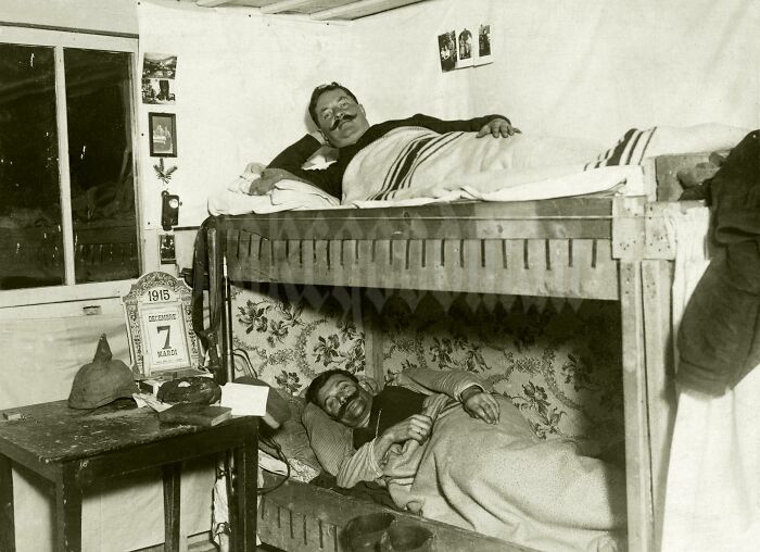 A historical photo of two men with moustaches resting in bunk beds, with a calendar showing March 7, 1915.