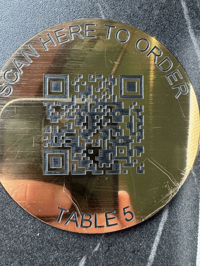 A gold disc with a QR code and text SCAN HERE TO ORDER TABLE 5. A construction fail.