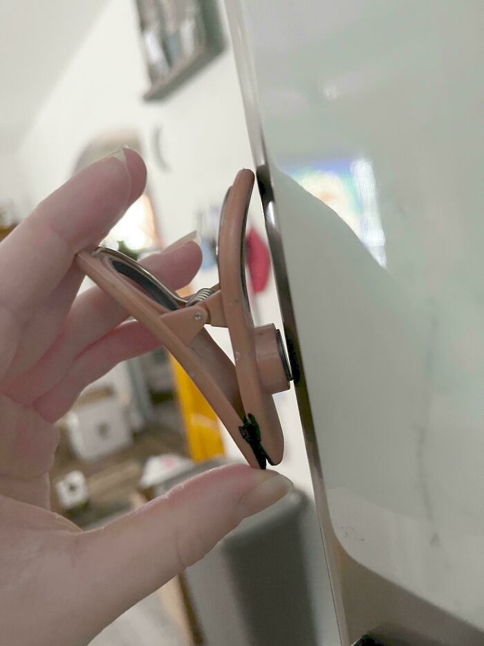 A hand holding a peach-colored chip clip, using it to hold something on a white surface, demonstrating a construction fail.