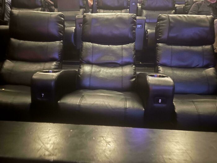 Empty black leather cinema seats with cup holders and seat numbers 7 and 8, revealing a construction fail.