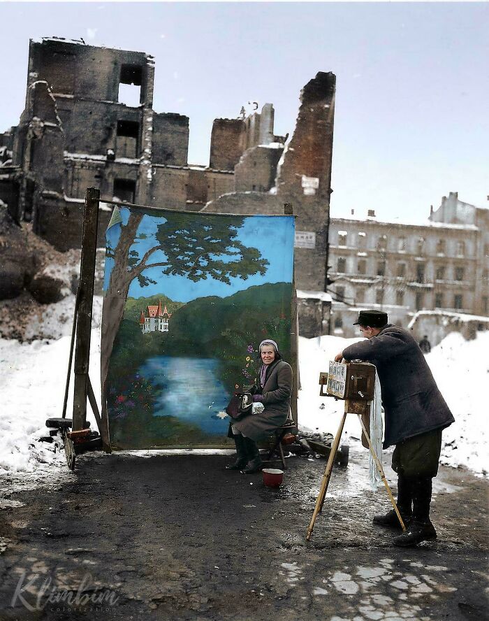 A photographer takes a portrait of a woman in front of a painted backdrop amidst snowy, war-torn ruins, from historical photos.
