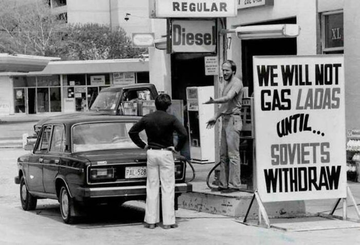 Historical photo of a man refusing to gas a Lada car with a sign that reads, WE WILL NOT GAS LADAs UNTIL SOVIETS WITHDRAW, a moment from the past.