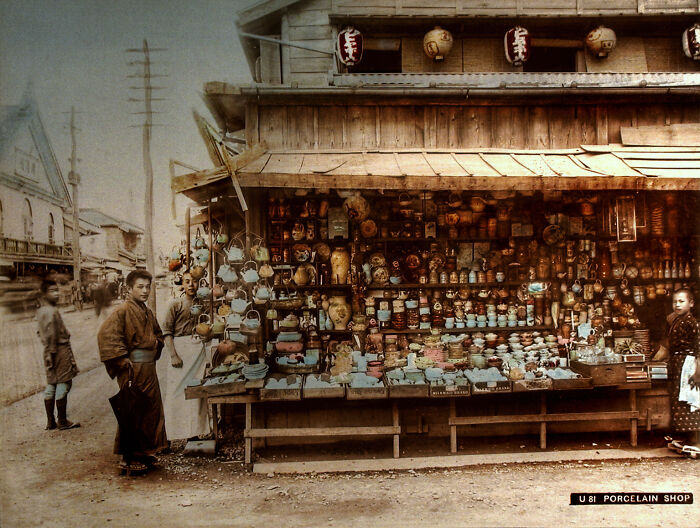 Historical photo of an old Japanese porcelain shop with detailed pottery and people outside, showing a vivid past.