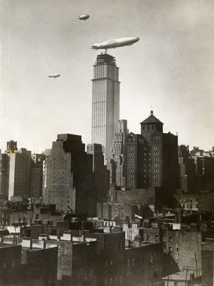 Historical photo showing three airships flying over skyscrapers in a bustling city, capturing a past moment.