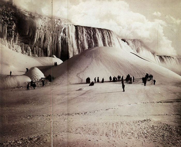 Historical photos: People walk on a snow-covered landscape with a frozen Niagara Falls in the background, a winter past.