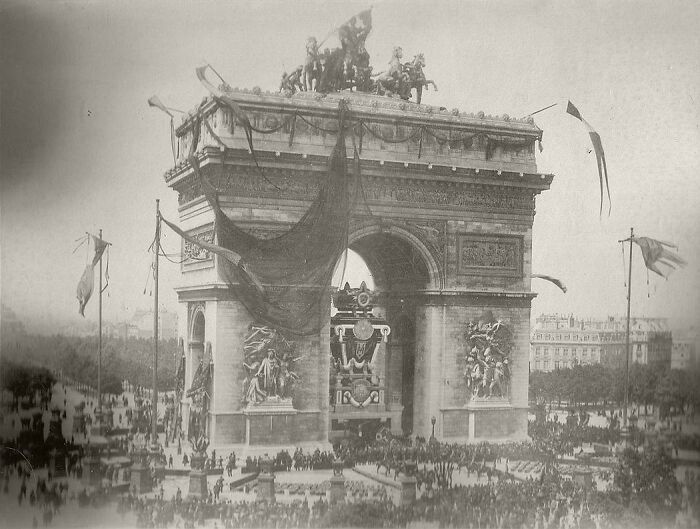 Historical photos: A large crowd gathers around the Arc de Triomphe, showcasing a past public event.