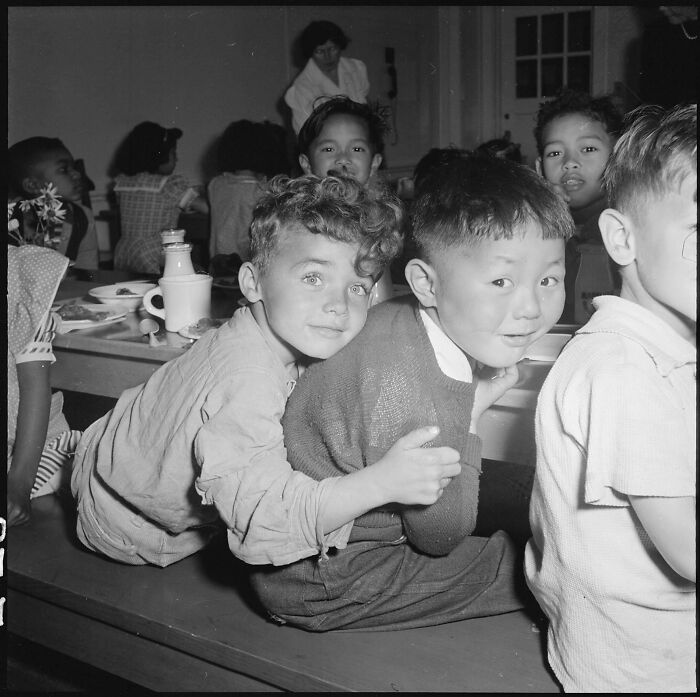 Two young boys embrace, looking at the camera, surrounded by other children, a historical photo showing a past moment.