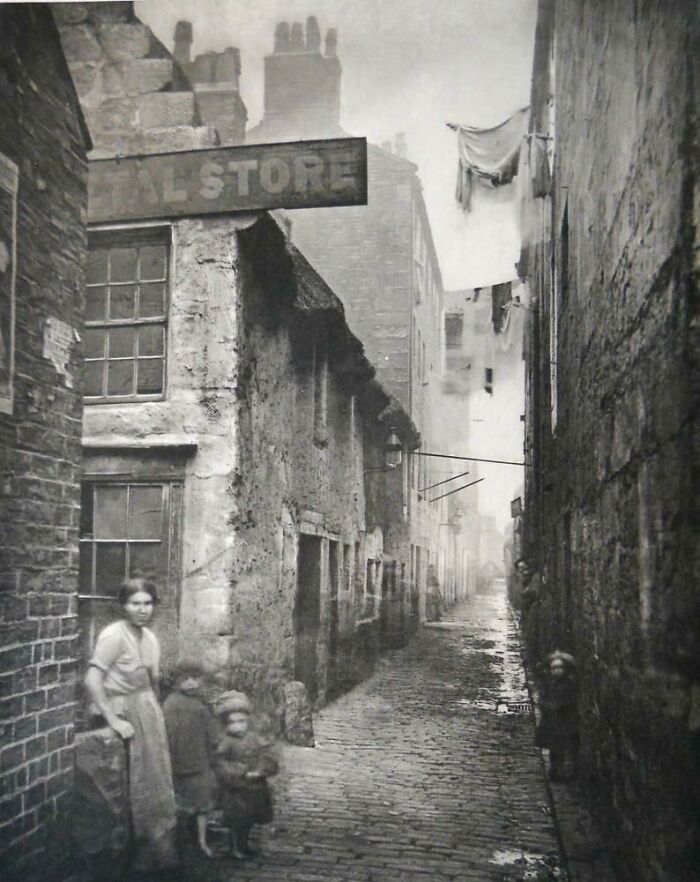 A narrow, cobbled street with old buildings and a small group of people, a historical photo capturing a past era.