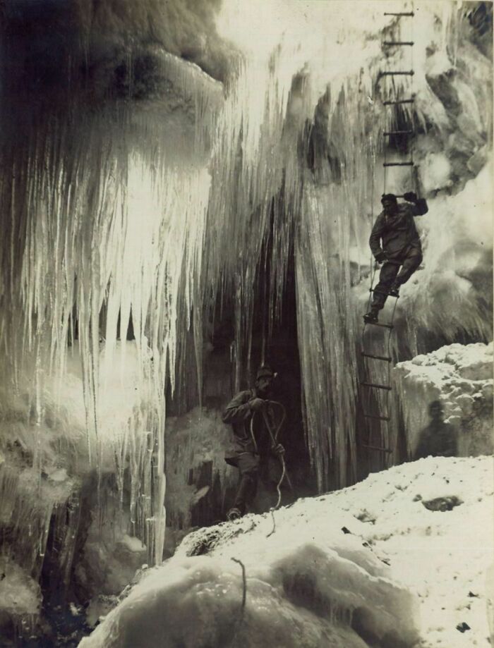 A historical photo of two climbers on an icy mountain, one ascending a ladder, documenting a challenging past expedition.