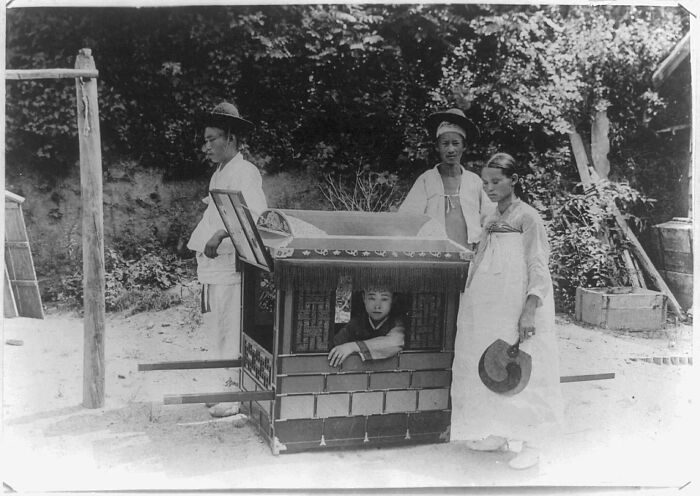 A captivating historical photo shows a child inside a palanquin, flanked by three adults in traditional clothing.