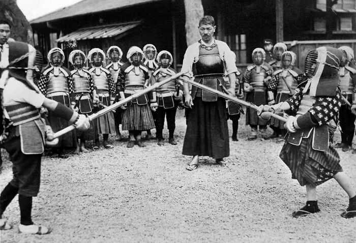 A black and white historical photo shows children in kendo armor practicing with swords, supervised by an adult.