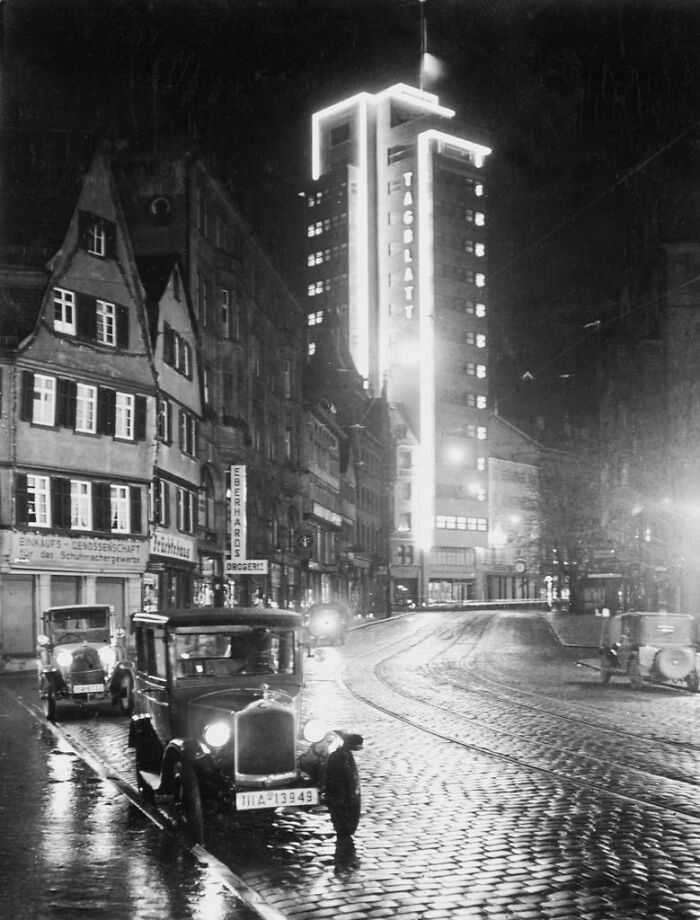 A street scene at night with vintage cars and a brightly lit building with the word TAGBLATT in a historical photo of a past city.