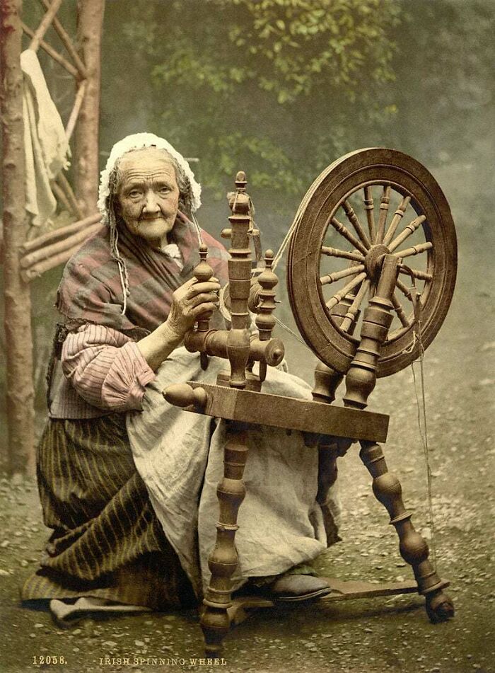 A historical photo of an elderly woman using a spinning wheel, illustrating a past craft and daily life.