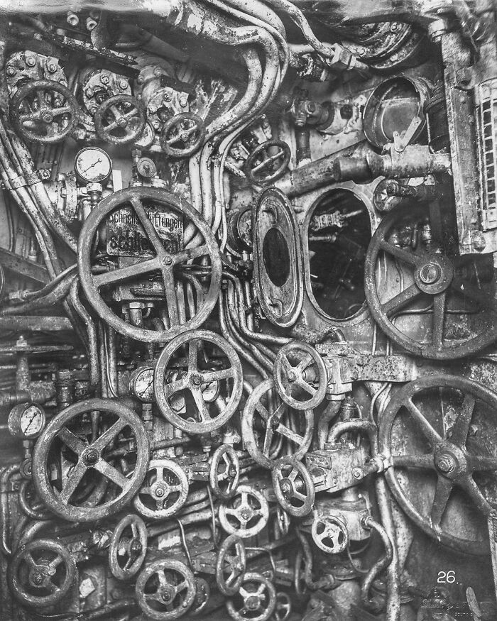 A complex historical photo shows the interior of a submarine with many wheels, gauges, and pipes, a past technological marvel.