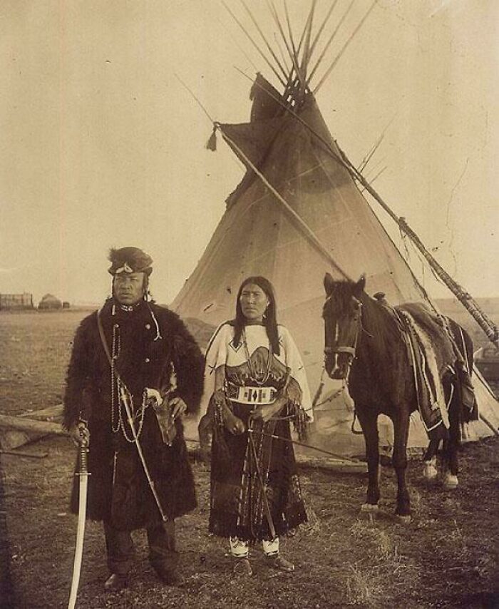 A historical photo shows a Native American couple in traditional attire with a horse and tipi, capturing a past moment.