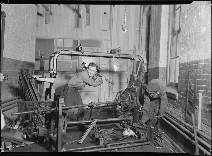 Two men working with tools on machinery in a historical photo of a workshop, showing a past moment in labor.