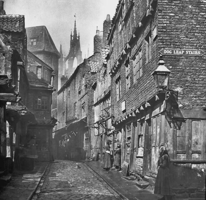 Historical photos of a narrow, cobbled street with old brick buildings and a distant spire.
