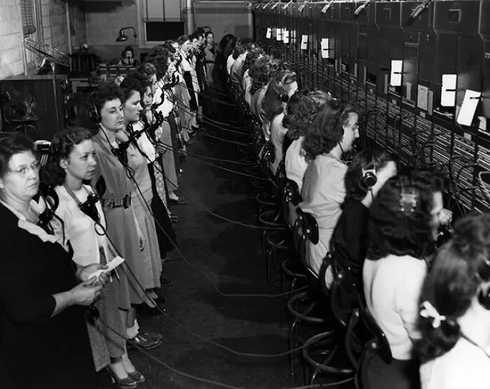 Historical photo of numerous women working at a switchboard, illustrating a past communication system.