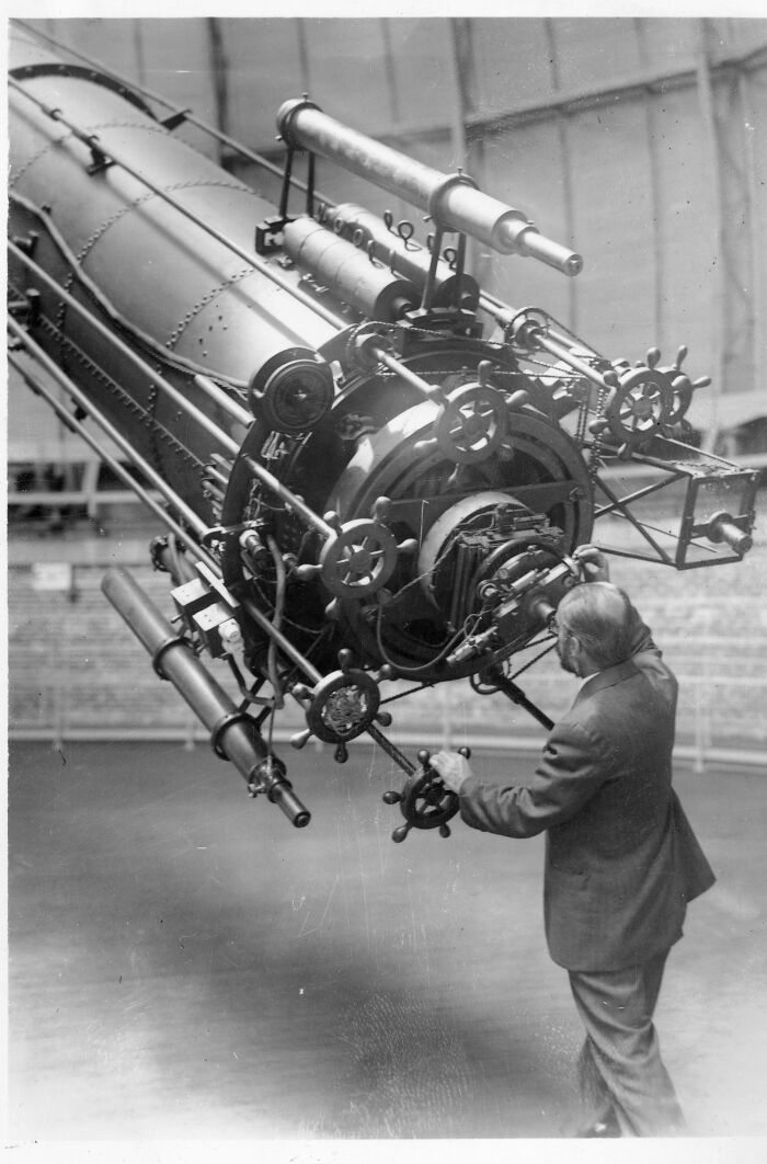 Historical photo of a man operating a large, intricate telescope, revealing a past scientific endeavor.