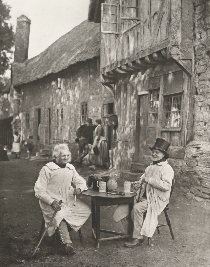 Historical photo of two men enjoying drinks outside a rustic building, depicting a past era.