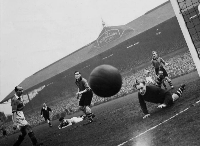Historical photo capturing a dynamic moment in a soccer match with players on the field and a stadium in the background.