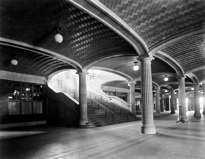 Historical photo of a grand interior with vaulted ceilings, pillars, and a sweeping staircase.