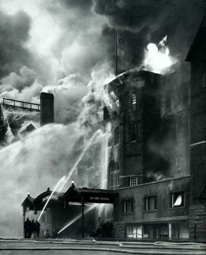 Historical photo of a building engulfed in flames, with firefighters battling the blaze.