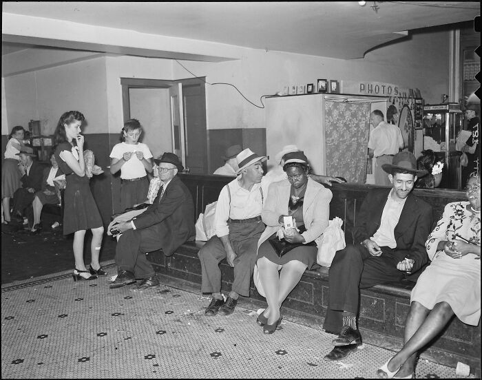 Historical photos: People gathered in a waiting room, some seated on benches, observing the scene, showing a past that will remain alive.