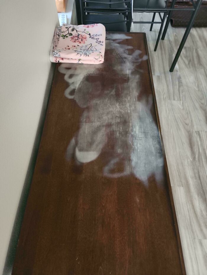 A long, wooden table with several white, ghostly marks, showing someone needs help fixing things, perhaps water damage.